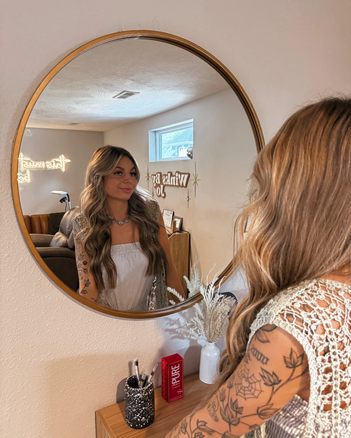 Jordan in the round brass mirror in her lash room, the Winks by Jo sign behind her